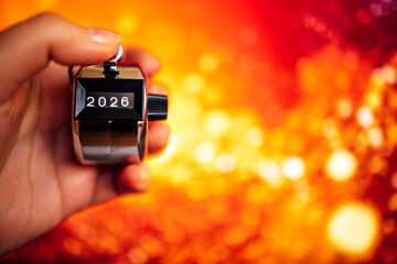 Hand holding a mechanical counter displaying the number 2026 against a vibrant, blurred background of warm colors, symbolizing the passage of time and future possibilities