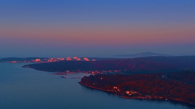 Twilight Coastline with Sunset Over Lake and Forested Hills. Aerial view of a serene coastal landscape at twilight, with a calm lake reflecting the pink and purple sky.