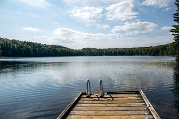A wooden dock with a metal ladder extending over the calm water of a forest lake in La Mauricie National Park, Quebec © Andrei Antipov