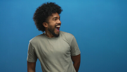 Man with curly hair smiling and pointing against a vibrant blue background exudes confidence and joy