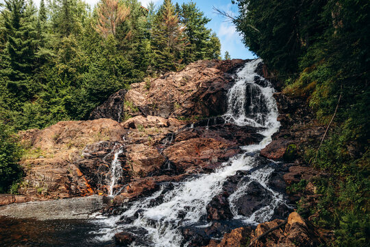 Scenic waterfall flowing over rocky terrain in Parc des Chutes de la Petite Riviere Bostonnais in Quebec, surrounded by lush evergreen forest and natural landscape.