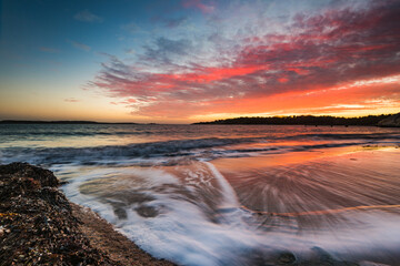 Colorful sunset at beach outside Gothenburg city with waves gently rolling on the shore