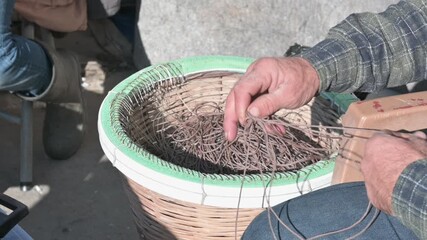 Detailed close-up shot of a fisherman working with his hands to repair tangled fishing line in a wicker basket. Authentic craftsmanship, traditional fishing skills and manual labor captured in natural