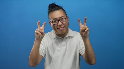 Fototapeta premium Young man making air quotes with raised fingers and wearing white polo in blue studio; playful sarcasm.