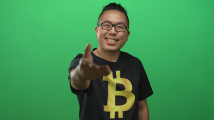 Man wearing bitcoin t shirt extends hand toward camera and smiles in green studio; trust invitation.