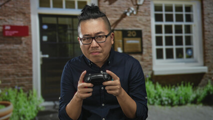 Man holds a game controller at a building entrance, hands gripping the controller with a tense focused expression; concentration.