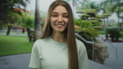 Teenage girl face with green shirt smiling and looking at camera outdoors by building; simple...