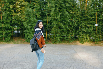 Naklejka premium Woman with backpack walking on a paved path beside green trees, casual style, cheerful pose, outdoor lifestyle and travel vibe for everyday moments