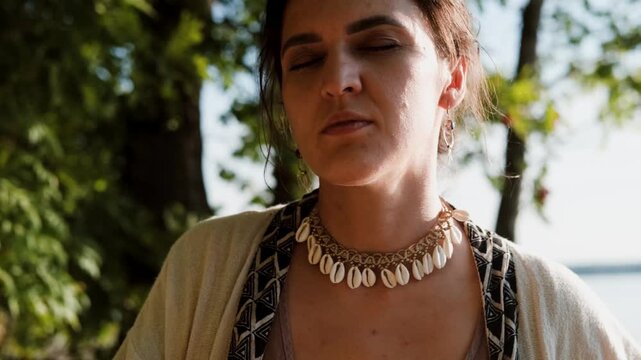 A beautiful brunette dressed in boho style meditates and dances in the forest. A magical ritual takes place against a green forest backdrop.