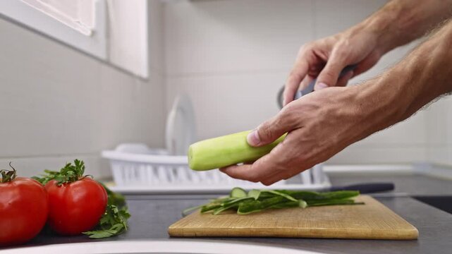 Close-up shot of hands peeling a fresh green cucumber with a peeler in a clean, modern kitchen. This highlights the importance of healthy food preparation and a fresh diet.