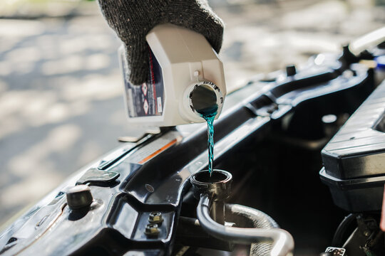  close-up  of a mechanic pouring coolant into the car's radiator for the engine's cooling system. Concepts of car repair and maintenance.