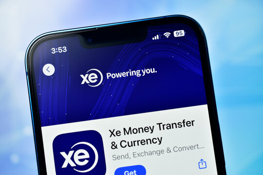 Closeup of xe money transfer currency app on smartphone screen against blue sky background