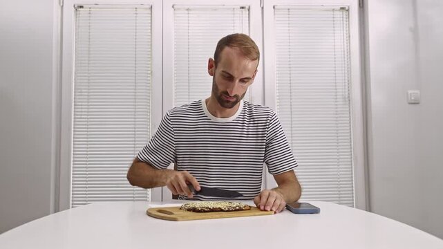Watch a man's humorous struggle to slice a seemingly indestructible healthy nut and seed bar. This everyday moment captures the challenge of preparing tough food at home with a blunt knife.