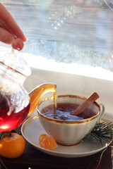 Tea from a transparent teapot is poured into a mug near the window. New Year's atmosphere