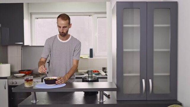 A young man enjoys a healthy breakfast meal in his modern kitchen. He is seen eating and savoring the nutritious food, representing a balanced lifestyle at home.