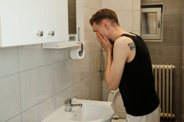 A man washes his face over the sink in a tiled bathroom. The concept shows refreshing morning...