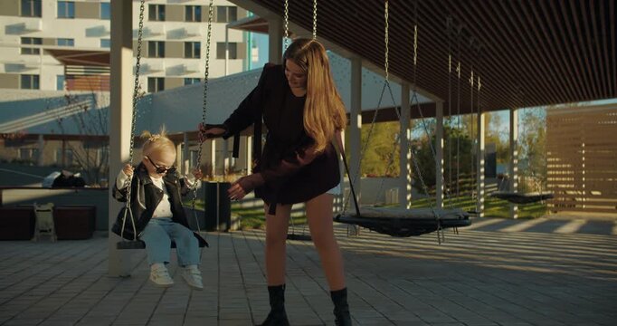 Woman pushing child on swing at modern playground