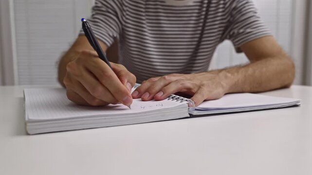 A student or professional diligently writes notes and solves mathematical problems in a spiral-bound notebook. This close-up footage highlights focus and concentration on a task.