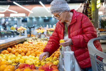Active Senior Woman's Winter Grocery Shopping: Choosing Fresh Citrus Fruits and Lemons for Vitamins and Immunity. Independent Elderly Lifestyle and Seasonal Food Selection in Supermarket.