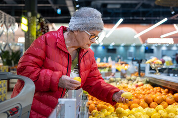 Active Senior Woman's Winter Grocery Shopping: Choosing Fresh Citrus Fruits and Lemons for Vitamins and Immunity. Independent Elderly Lifestyle and Seasonal Food Selection in Supermarket.