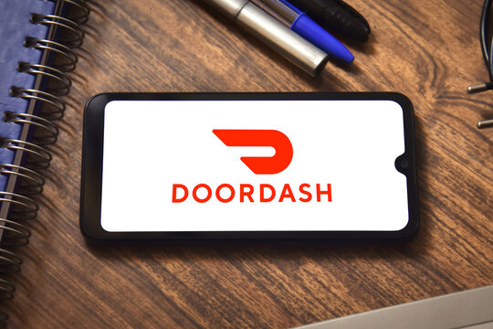 DoorDash logo on a smartphone screen with office supplies in the background. Concept of online delivery and ordering.