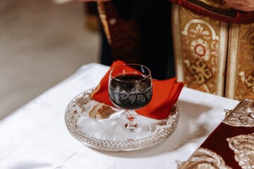 Close-up of a glass of red wine and bread on a silver tray during an Orthodox wedding ceremony, symbolizing the common cup.