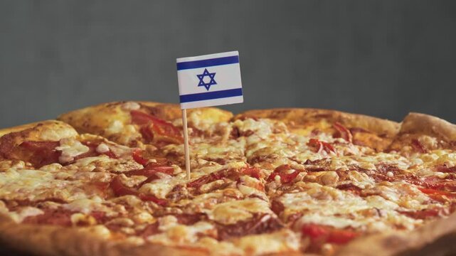Slowly rotating cheese pizza with Israeli flag inserted into slice, scene emphasizes local Israeli dairy and wheat used for kosher style pizza.