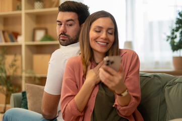 Suspicious man looking at woman secretly using smartphone