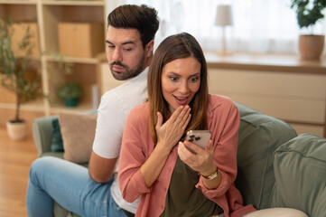 Man feeling suspicious while woman reacting with shock to phone