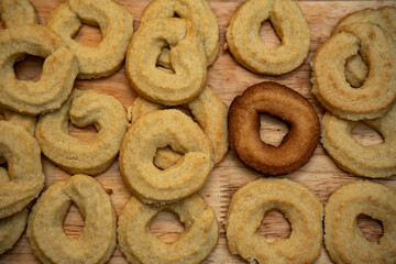 Freshly baked traditional Scandinavian Danish Christmas cookies called Vanilla rings, laying on wooden surface. One over baked black cookies sticks out, diversity and exclusion concept.