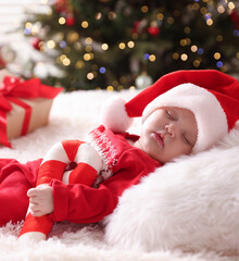 Cute little baby in Santa hat with festive decor sleeping on bed at home. Christmas season