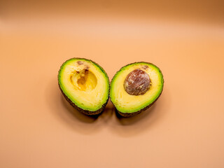 Halves of ripe avocado on a beige background, one with the pit and one with an empty seed cavity.