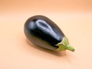 Whole eggplant lying at a slight angle on a plain beige background &ndash; simple product shot.