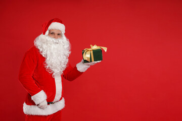 Santa Claus with Christmas gift on red background, space for text