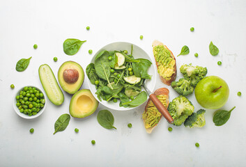 Fresh salad bowl, avocado toasts, raw green vegetables fruit white background top view, diet