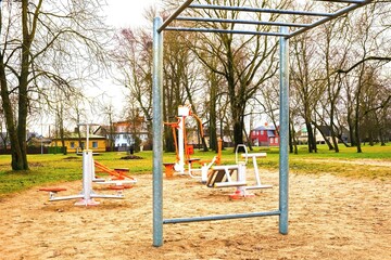 Outdoor gym equipment on empty sandy sports ground in city park, public street workout area with exercise machines and pull up bars, healthy lifestyle and fitness concept in residential neighborhood.