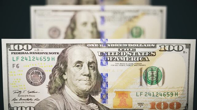 Close-up of American 100 dollar bills moving in a continuous stream. Seamless loop 4K animation on a dark background.