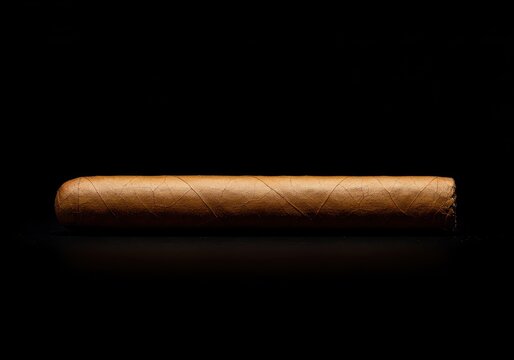 A single premium cigar resting horizontally against a deep black backdrop, emphasizing texture and contrast ,Cigar ,tobacco ,isolated.