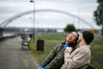 Happy couple laughing while relaxing on a bench in park