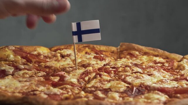 Rotating tomato cheese pizza with Finnish flag on toothpick, frame hints at use of Finnish milk cheeses and local grain for crust.