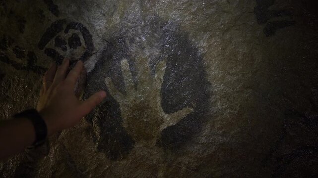 Explorer Touching Ancient Cave Painting on Rock Wall