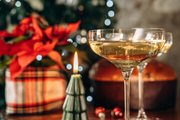 Two elegant champagne glasses filled with bubbly drink, placed on wooden table, with a beautifully decorated Christmas tree in the background