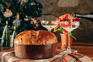 traditional Italian Christmas bread Panettone cake with sparkling wine or champagne in elegant glasses on a decorated table for a festive lunch or dinner, New Year Christmas food tradition