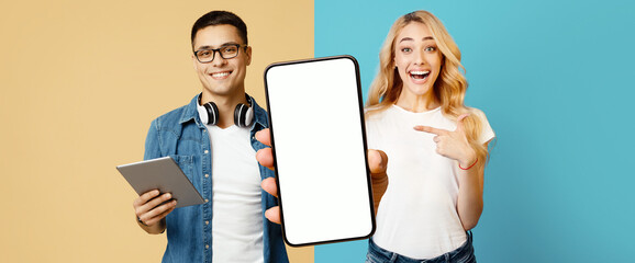 A young man with glasses holds a tablet while a woman points at a blank phone. They both display...
