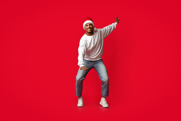 A man dressed in casual attire, including a santa hat, demonstrates festive spirit while dancing on...