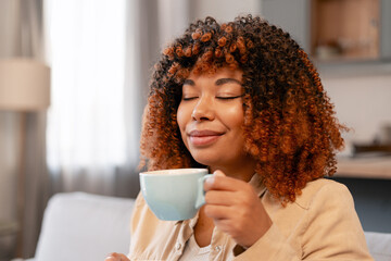 Young black woman enjoying coffee or tea at home, closing eyes and smiling