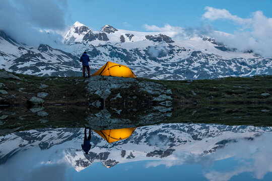 Trekker accanto a tenda illiminata riflessi sul lago, con Monte Rosa sullo sfondo, campeggio selvaggio (wild camping), valtournenche, Italia