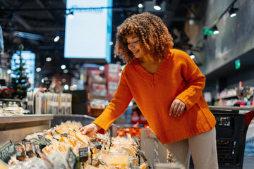 Happy black woman choosing cheese in supermarket, enjoying grocery shopping