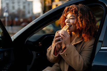 Young woman enjoying a quick lunch in car, eating fast food on the go, smiling