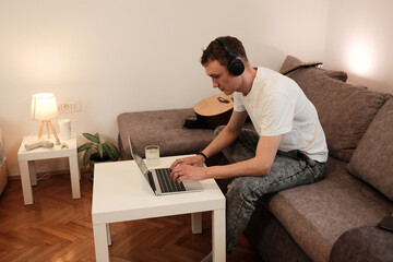 Fototapeta premium A man works on his laptop while sitting on the sofa. The concept reflects productivity and remote work in a relaxed home environment.